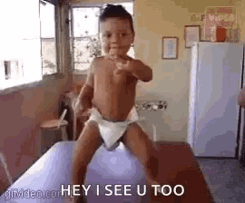 a baby in a diaper is standing on a table and pointing .