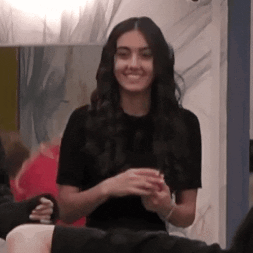 a woman in a black t-shirt is smiling in front of a mirror in a room .