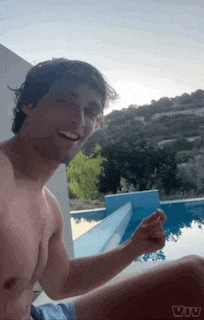 a shirtless man is taking a selfie next to a swimming pool