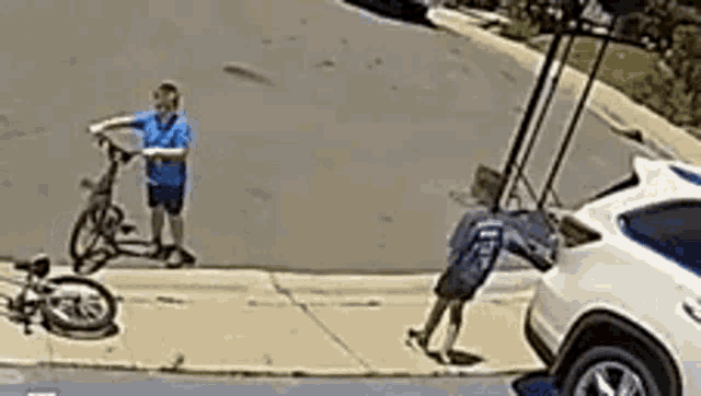 a boy is riding a bike down a sidewalk next to a white car .