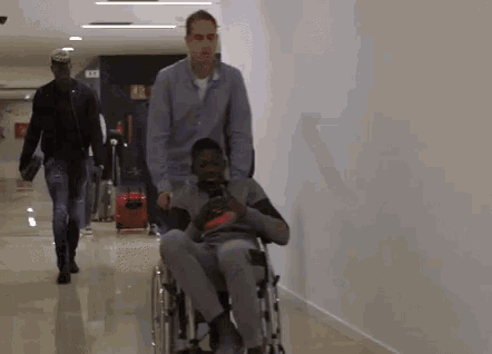 a man is pushing another man in a wheelchair down a hallway