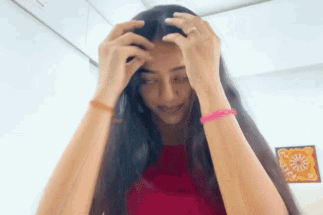 a woman with long hair is holding her head with her hands and wearing bracelets on her wrists .