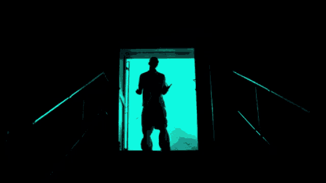 a silhouette of a man walking through a doorway with a green light behind him