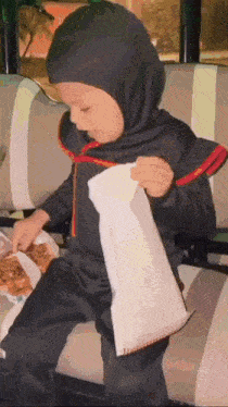 a little boy dressed in a ninja costume is sitting on a couch eating food .
