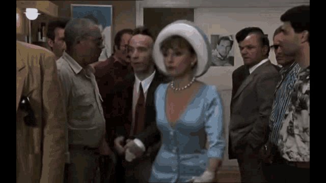 a woman in a blue dress and white hat is surrounded by men in suits and ties