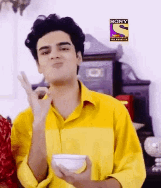 a man in a yellow shirt is holding a bowl and making a face .