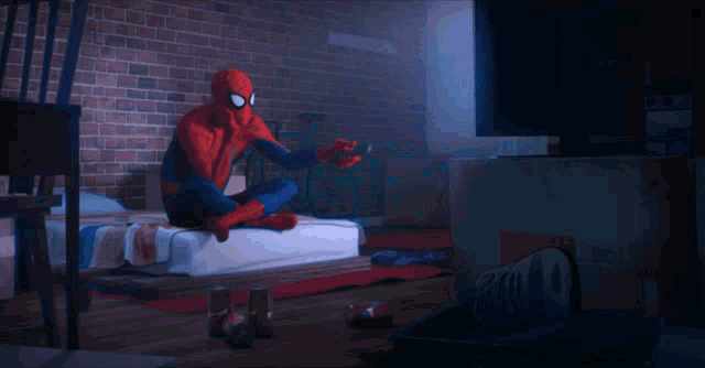 a spider man is sitting on a bed holding a controller