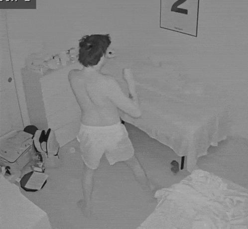 a black and white photo of a shirtless man in a bedroom with the letter n hanging on the wall