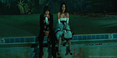 a man in a tuxedo and a woman in a dress are sitting on the edge of a pool .