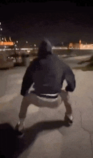a man in a hoodie is doing a squat on the ground at night .