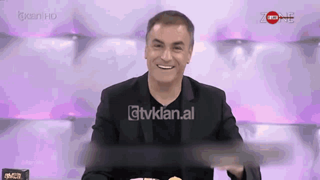 a man in a suit is smiling in front of a screen that says zone