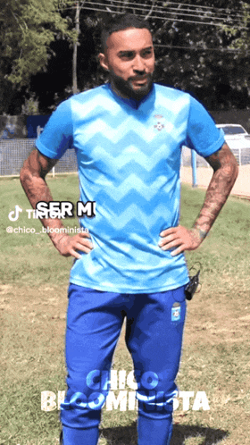 a man in a blue shirt and blue pants is standing on a field with his hands on his hips