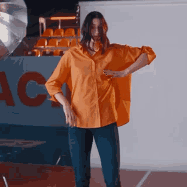 a woman in an orange shirt is dancing in front of a sign that says ac on it