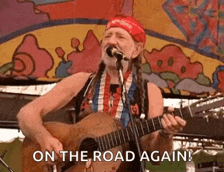 a man is playing a guitar and singing into a microphone while on the road again .