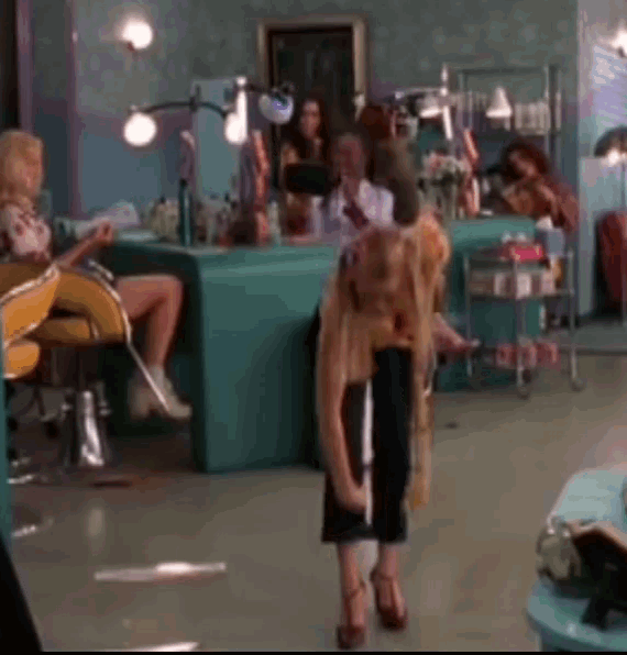 a woman is standing in a hair salon while a man sits in a chair