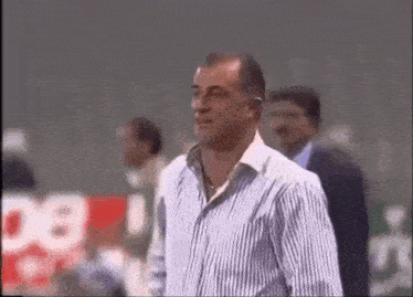 a man in a striped shirt is standing in front of a sign that says ' bb ' on it .