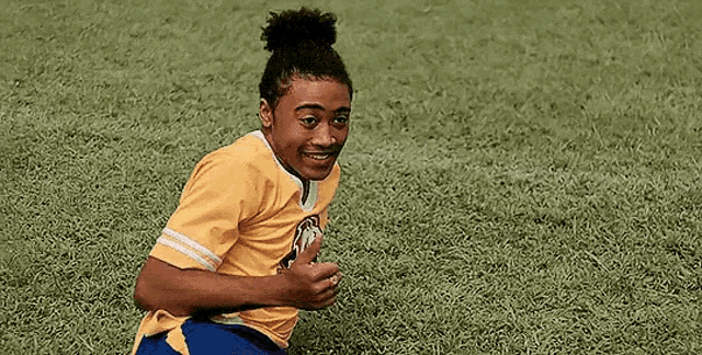 a young man in a yellow shirt is kneeling on a soccer field .
