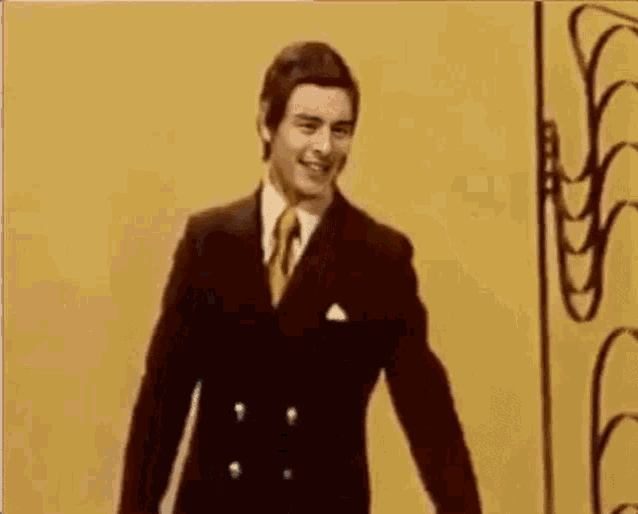 a man in a suit and tie is standing in front of a yellow wall and smiling .