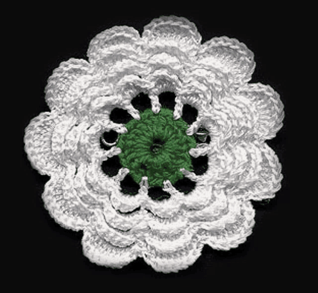 a white crocheted flower with a green center is sitting on a black surface .