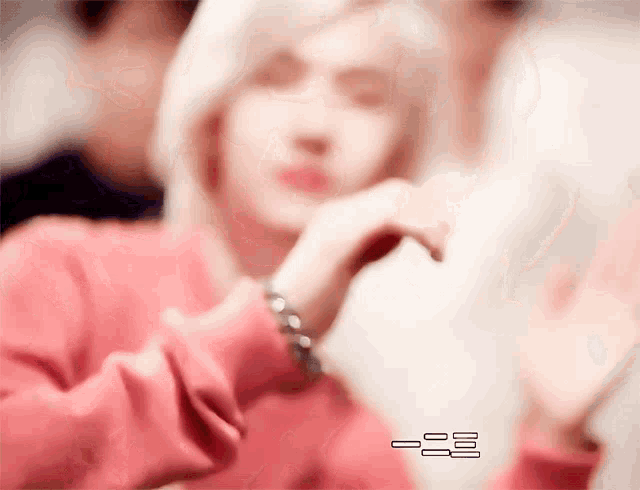 a blurry picture of a woman wearing a pink sweater with a bracelet on her wrist