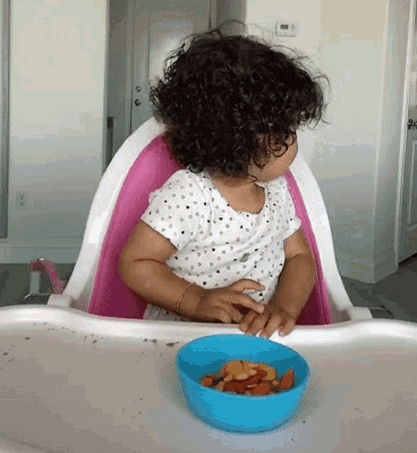 a little girl is sitting in a high chair with a bowl of fruit