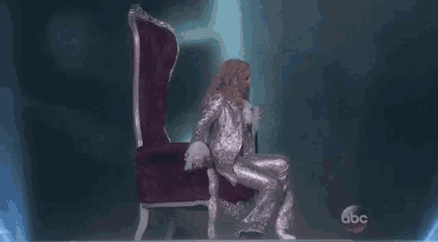 a woman in a purple suit is sitting in a purple chair on a stage .