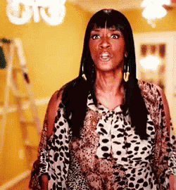 a woman in a leopard print shirt is standing in a room with a ladder in the background .