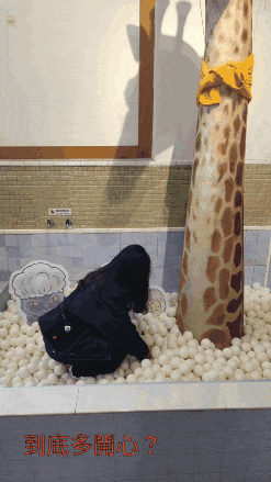 a woman playing in a pool of white balls with a giraffe in the background
