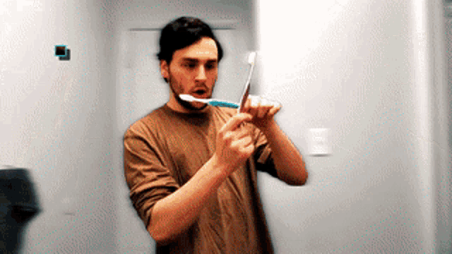 a man in a brown shirt is brushing his teeth in front of a mirror