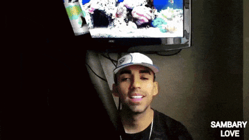 a man wearing a hat is smiling in front of a tv screen that says sambary love on it
