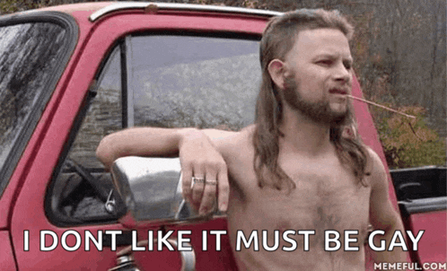 a shirtless man with a mullet is leaning on the back of a red truck and smoking a cigarette .