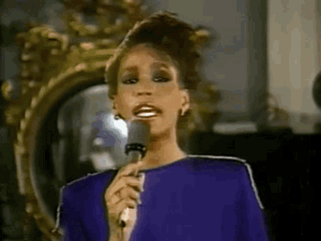 a woman is singing into a microphone while wearing a purple dress .