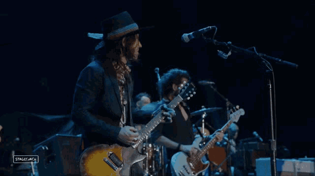 a man playing a guitar in front of a microphone with stagecoach in the corner