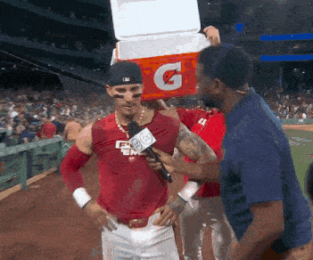 a baseball player is being interviewed by a reporter while holding a gatorade cooler on his head