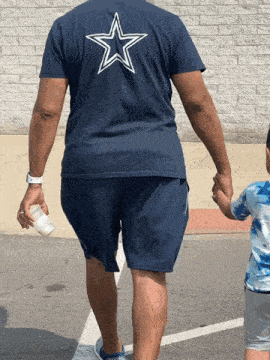 a man wearing a blue shirt with a white star on the back is holding a child 's hand