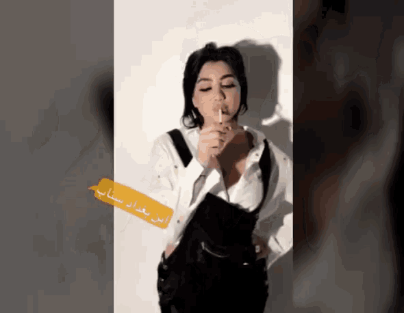a woman smoking a cigarette in front of a white wall with arabic writing on it