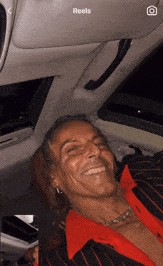 a man in a red and black striped shirt is sitting in the back seat of a car with the word reels on the screen