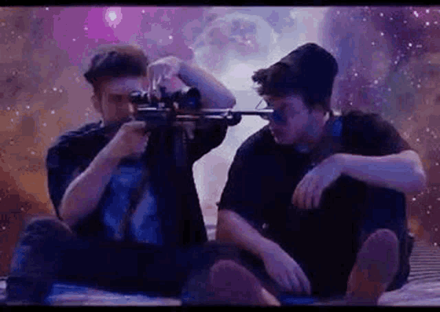 two men are sitting on a bed holding guns in front of a galaxy .
