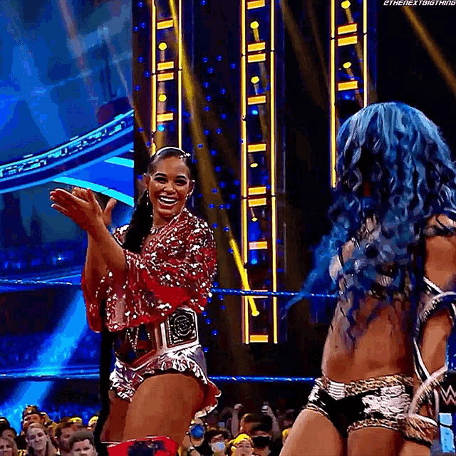 two female wrestlers are standing in a wrestling ring applauding the crowd .
