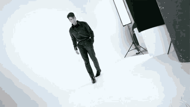 a man in a black shirt and black pants is walking on a white surface