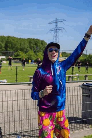 a man wearing a hoodie and pineapple shorts stands in a field
