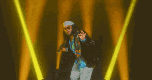 a man wearing sunglasses and a hat is dancing in front of a yellow light