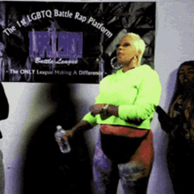a woman in a neon green sweater stands in front of a sign that says the 1st lgbtq battle rap platform