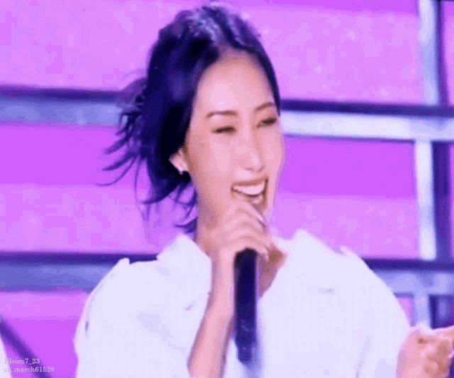 a woman is singing into a microphone on a stage while wearing a white shirt .