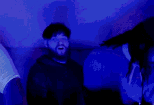 a man with dreadlocks is standing next to another man in a room with blue lights .