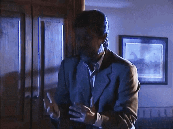a man in a suit is standing in a dark room smoking a cigarette