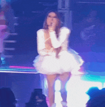 a woman in a white dress singing into a microphone on a stage