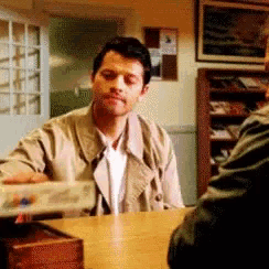 a man in a trench coat is sitting at a table with another man