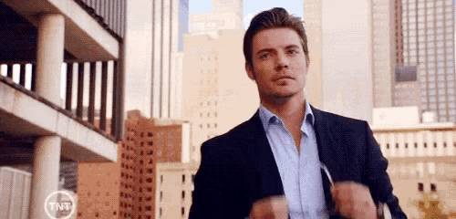 a man in a suit and blue shirt is standing in front of a city .
