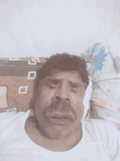 a man with a mustache is laying on a bed with his eyes closed and his shirt says pmn
